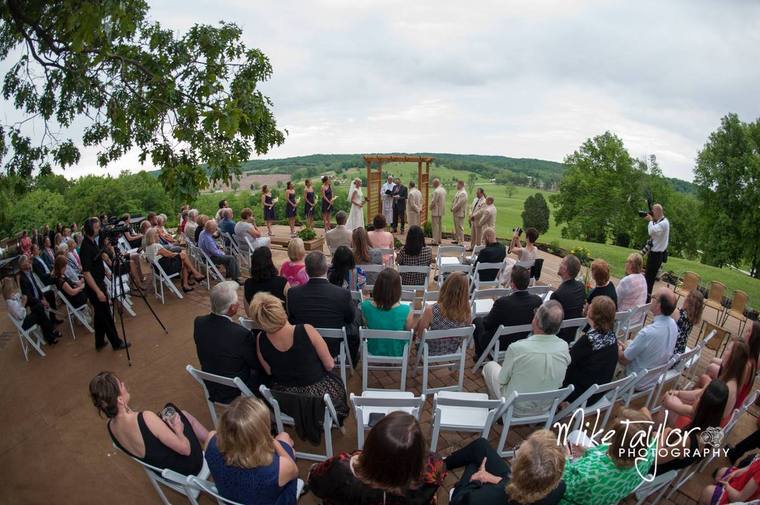 A hilltop ceremony under way, guests seated facing the arbor with the valley beyond
